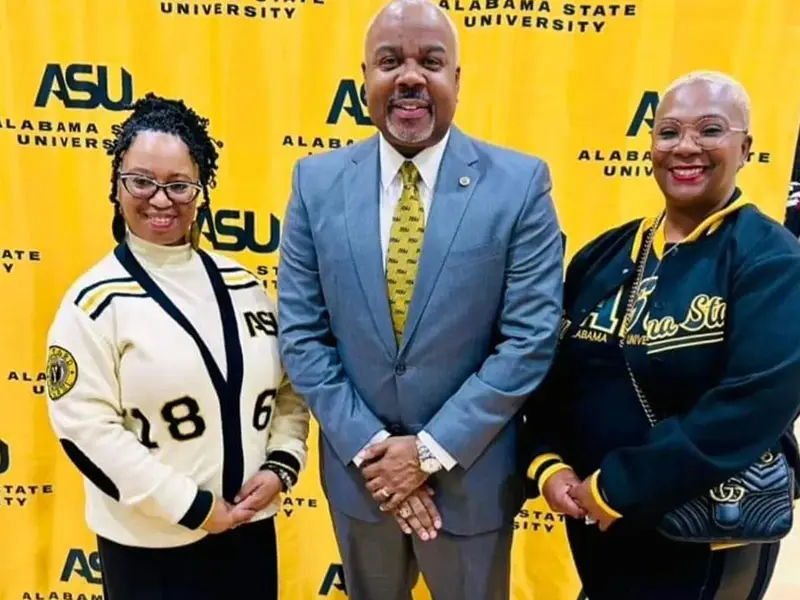 Three people standing in front of a yellow background.